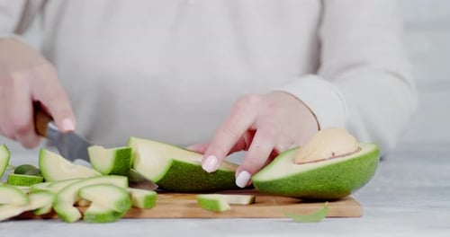 Woman Slices Fresh Avocado on Cutting Board