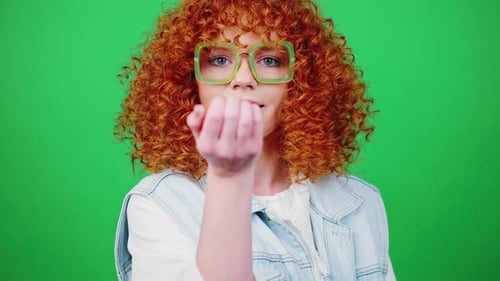 Young Playful Redhead Curly Woman Blowing Colorful Confetti to Camera Smiling Over Green Chroma Key