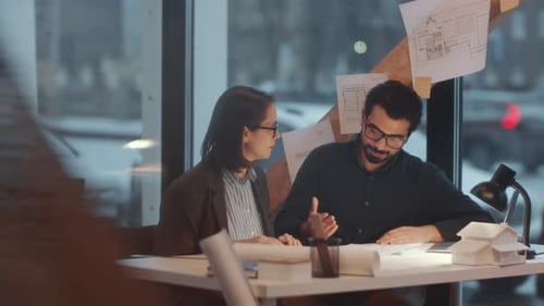 Male and Female Architects Discussing Blueprint at Office Desk