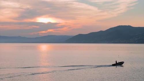 Dinghy moving from left to right at sunset, with mountains in the background and orange sky, shot ne