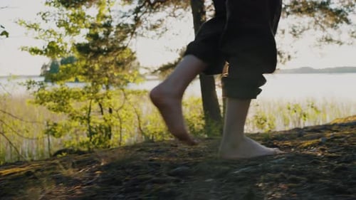 Side View of Female Bare Feet Walking Along a Rocky Shore Covered with Moss Against the Backdrop of