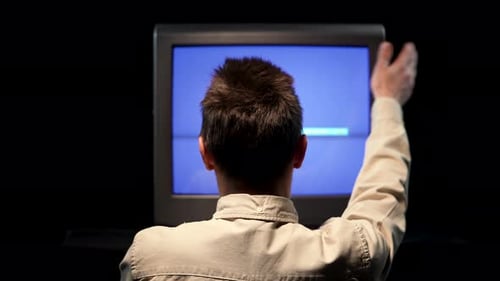 Rear View of a Man Sitting in Front of an Old TV with Noise Interference on a Blue TV Monitor in a