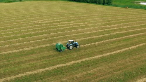Luftbildtraktor sammelt trockenes Gras in Strohballen im Weizenfeld