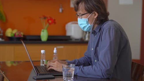 A Young Man Wearing a Face Mask Works From Home During Corona Virus Self Isolation