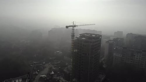 Birds eye view on tower crane in fog standing next to residential building.