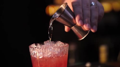 Hand Pours Cocktail Ingredient into Icy Glass