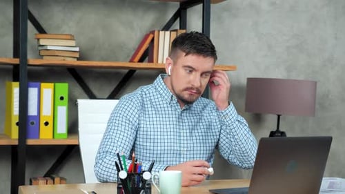 Business man in home office puts on wireless earphones starts using laptop