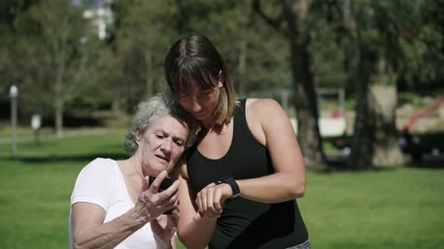 Senior Woman and Young Woman Looking at Phone Outdoors