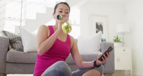 Woman Drinking Water and Using Smartphone Indoors