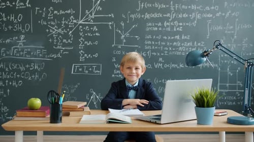 Portrait of Smiling Smart Boy at School Desk with Chalkboard with Formulas in Background
