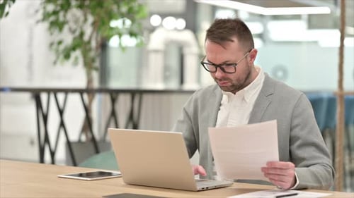 Man Reviews Documents While Typing On Laptop