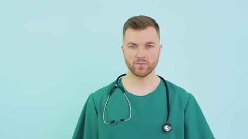 Erfolgreicher Doktor Chirurg in grünen Uniform blauen Handschuhen und Stethoskop schaut in die Kamera auf Blau