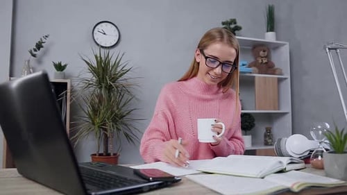 Blondes Mädchen im rosa Pullover schreibt notwendige Notizen aus Book Into Notebook