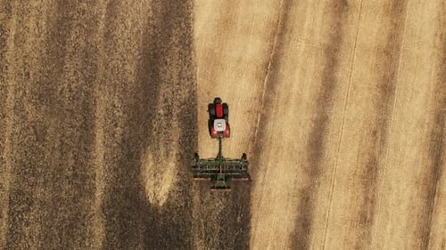 Tractor pulls a plow across a farm field. preparation of the field before sowing. Drone view