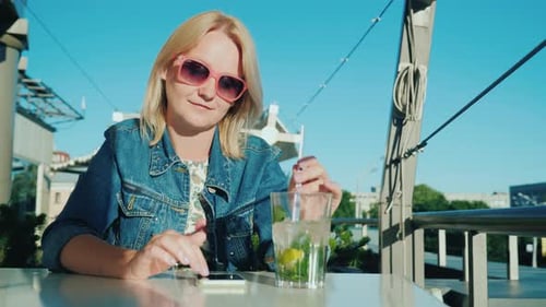 A Woman Uses a Smartphone, Resting in a Summer Cafe