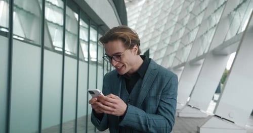 Excited man checks phone outside modern building
