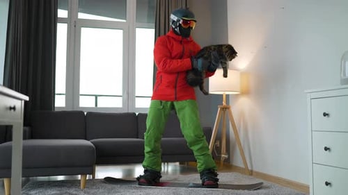 Snowboarder Holds Cat Indoors on Snowboard