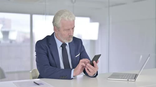 Old Businessman Using Smartphone in Modern Office