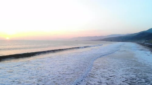 Luftaufnahme von Meereswellen, die am Strand unter einem farbenfrohen Hintergrund des Sonnenuntergangshimmels entlang der Küste krachen