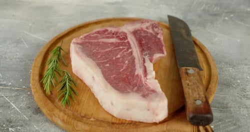 Steak de bœuf cru en forme de T avec couteau et romarin rotatif.