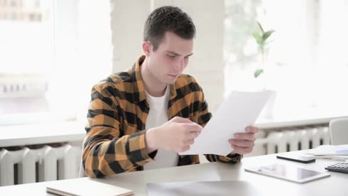Young Man Reviews Paperwork in Bright Office