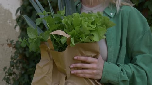 Mujer sonriente con verduras en bolsa sobre fondo de pared de hiedra