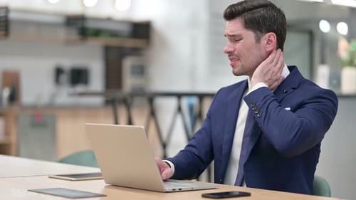 Tired Businessman with Laptop Having Neck Pain in Office