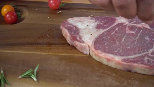 Chef cook season fresh chunk of deli piece of beef with sea salt and grounded spicy peppers.