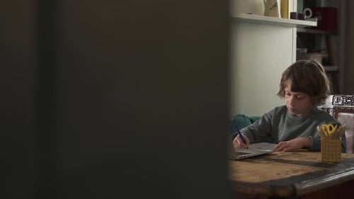 American School Boy is Writing in Notebook During Online Learning at Table in Apartment Spbd