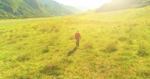 Flight Over Backpack Hiking Tourist Walking Across Green Mountain Field. Huge Rural Valley at Summer