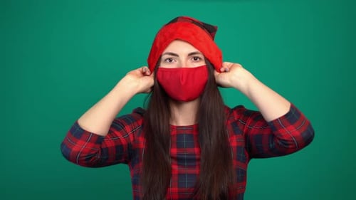 Frau trägt rote medizinische Gesichtsmaske, die eine Weihnachtsmütze aufsetzt.