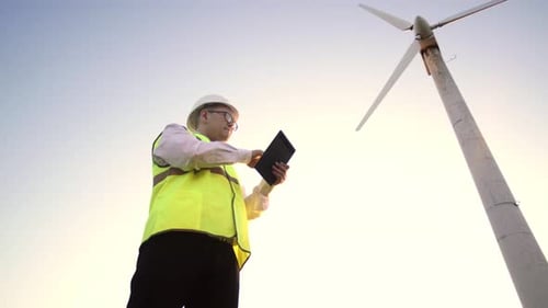 Engineer of Asian Appearance Is Near the Windmill and Keeps Working Tablet You Hands, Examining All