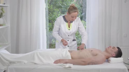 Plan large d'un médecin professionnel insérant des aiguilles dans le ventre d'un jeune homme faible. Sérieusement confiant