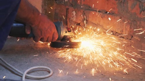 Worker is cutting metal with circular saw with sparks flying around