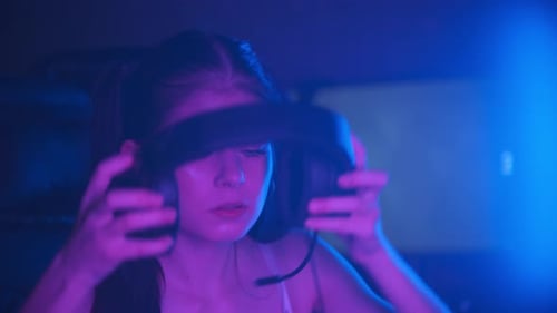 Young Attractive Woman Sitting in Neon Gaming Club and Putting on Big Headphones and Greeting Her
