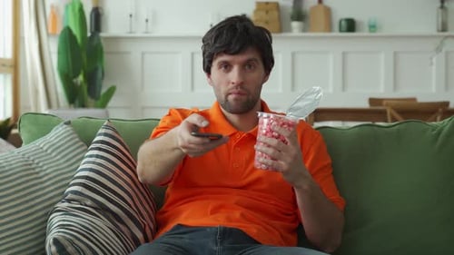 Man Sitting on Couch Eating and Watching TV