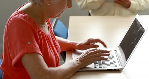 Older Woman Typing on Laptop, Man Uses Tablet