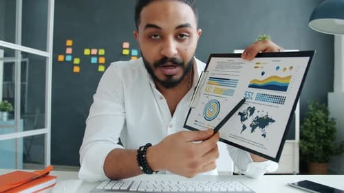 Portrait of Mixed Race Guy Talking and Showing Charts During Video Conference Online in Office