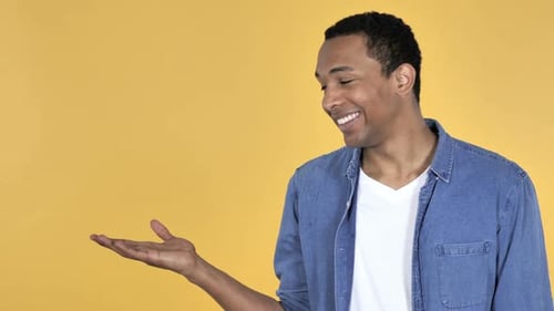 Young African Man Showing Product at Side Yellow Background