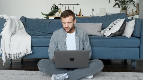 Man Works on Laptop from Home Sitting on Floor
