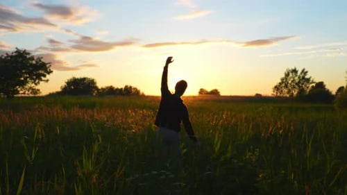 Silhouette of man doing stretching exercises in middle of fields during beautiful golden hour.