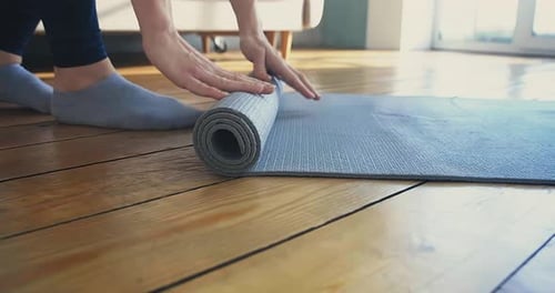 Woman Rolling Up Yoga Mat on Wooden Floor