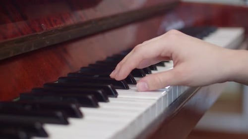 Hand plays keys on an upright piano
