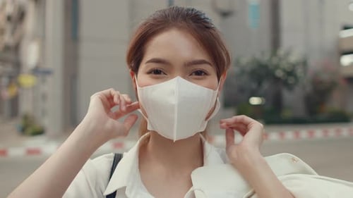 Businesswoman wear face mask smiling and looking at camera while happy alone outdoors in city