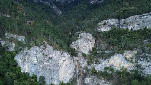 Aerial footage of a waterfall in rocky green forests high at the mountains