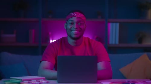 Young Adult Smiling with Laptop in Neon Lit Room
