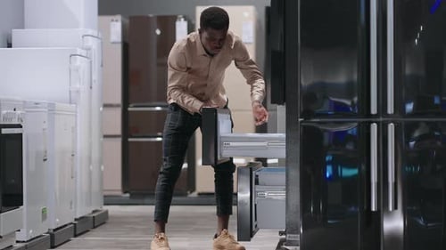 Afroamerican Man is Choosing Fridge in Home Appliance Store Viewing Exhibition Sample Inside Opening