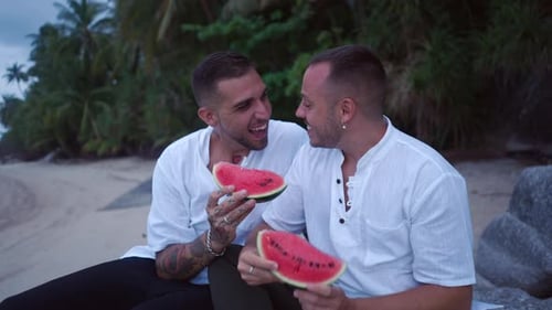 Casal homossexual se divertindo comendo melancia na praia à noite