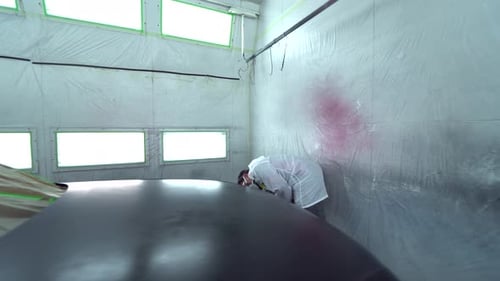 Car body painter spraying car in paint booth