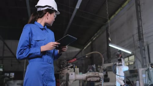 Asian factory worker woman inspect the industrial robot arm machine by using the tablet